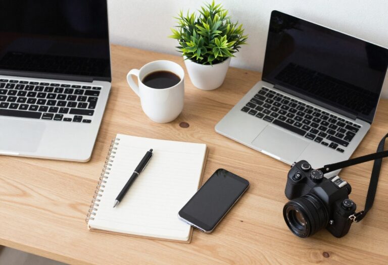Weekend side hustle essentials including laptop, coffee, notebook, phone, dog leash, and camera on a wooden table.