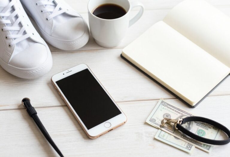 Weekend side hustle essentials including smartphone, coffee, notebook, sneakers, pet leash, and cash on a wooden table.