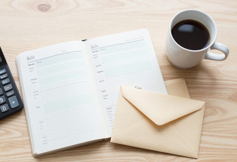 Flat lay of payday budgeting essentials: paycheck, calculator, notebook, envelopes, and coffee on a wooden desk.