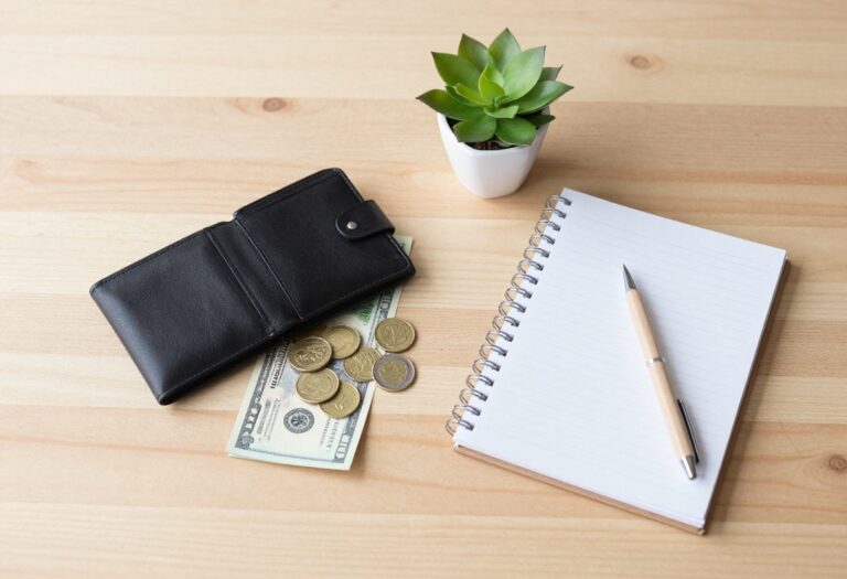 Flat lay of wallet, cash, coins, notepad, and plant on wooden table